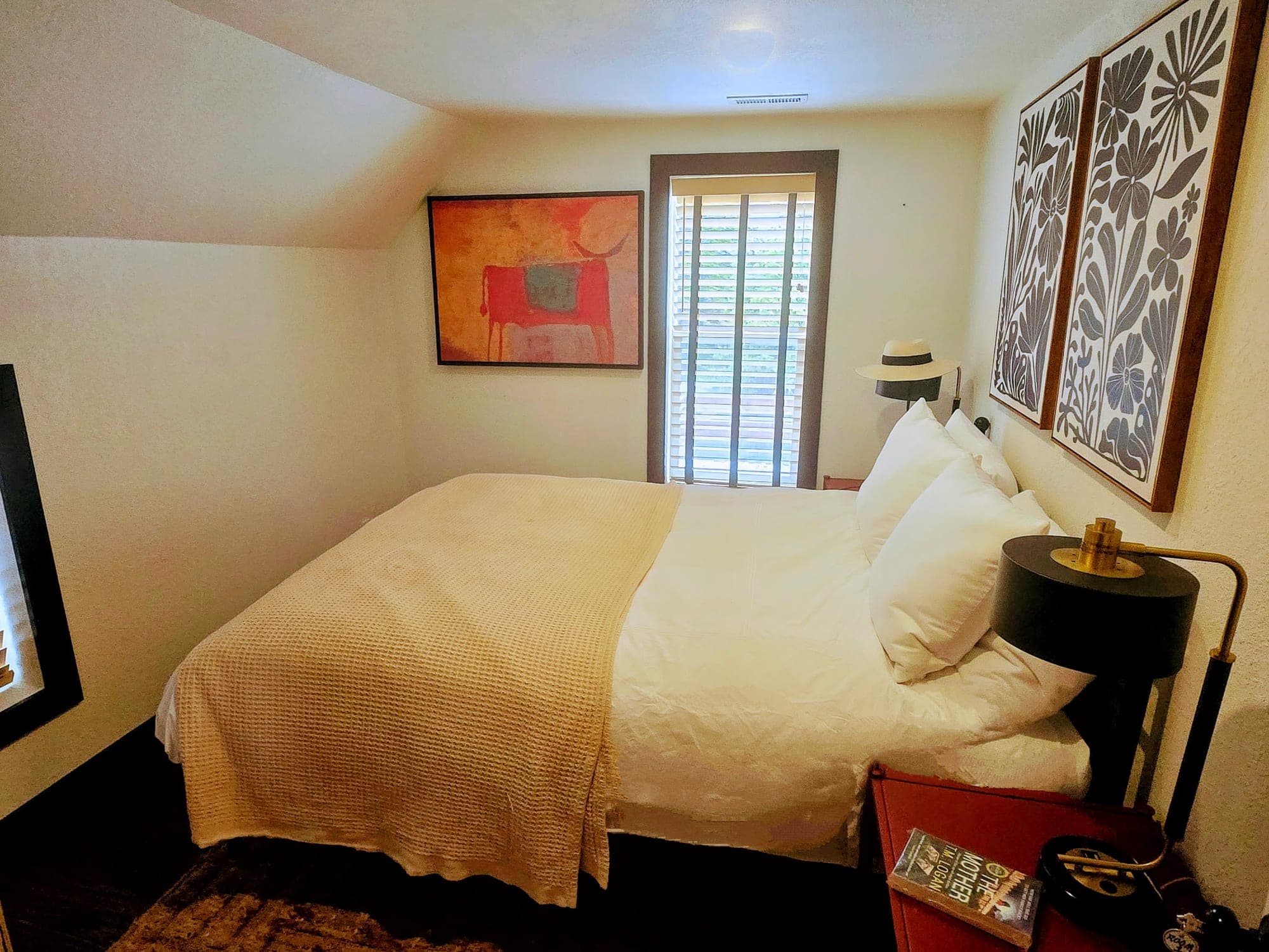 Queen bedroom in The Tavern Loft with white linens, a red horse painting, and a sunlit window