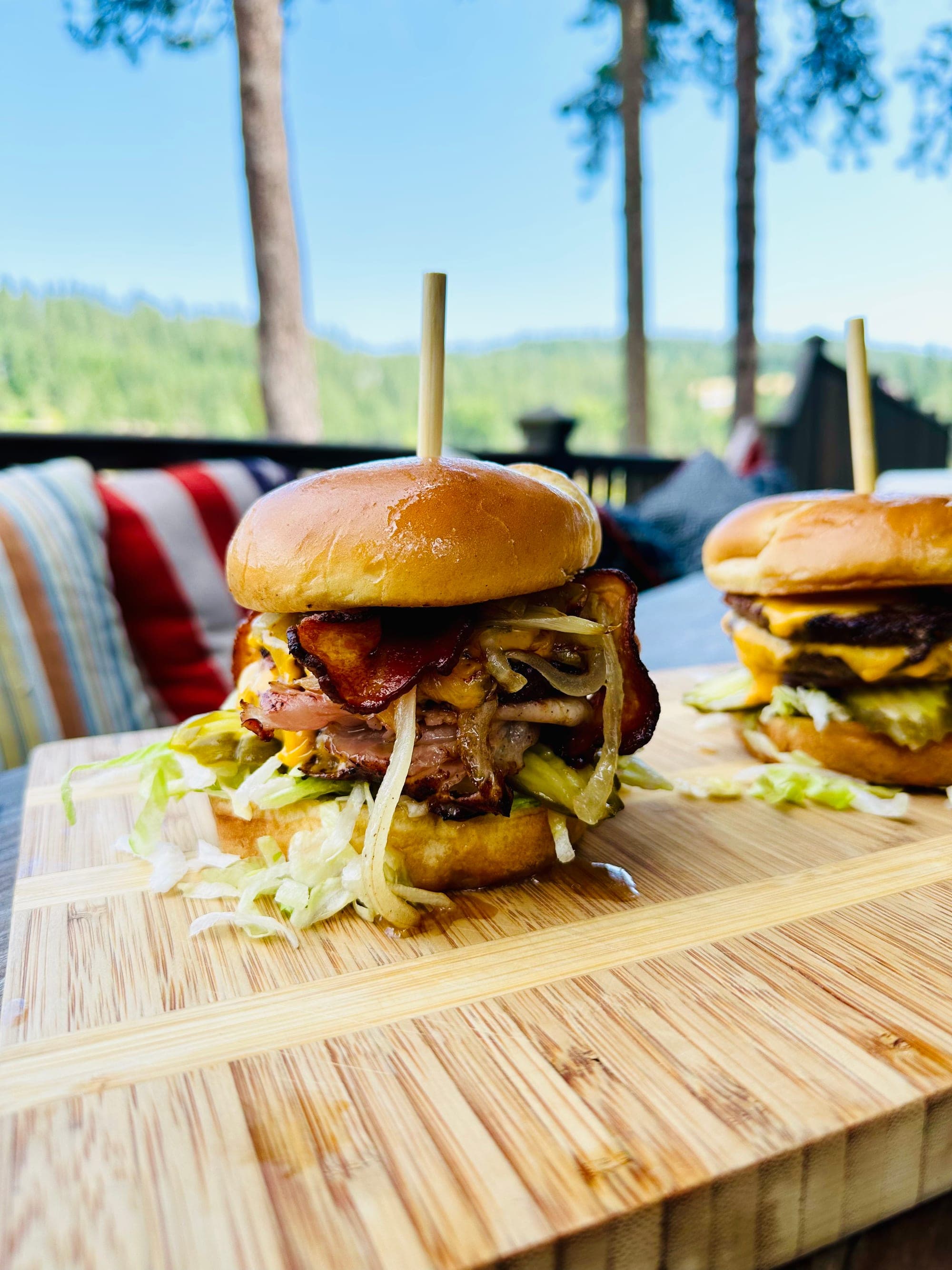 Stacked bacon burgers on a wood board with the deck and forest view at Red's Tavern