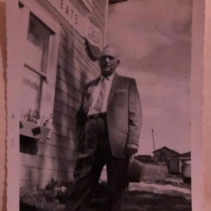 Sepia-toned archival photograph of a man in a suit beside the historic 'EATS' diner storefront on the Watson's property